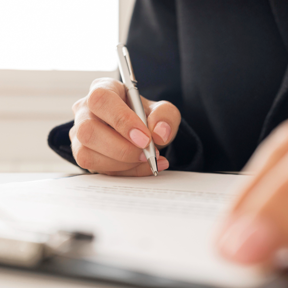 Mano firmando un documento sobre una superficie de trabajo.